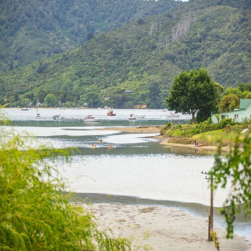 A portrait photo of a landscape depicting water flowing through sandy banks with hills in the background covered in trees.